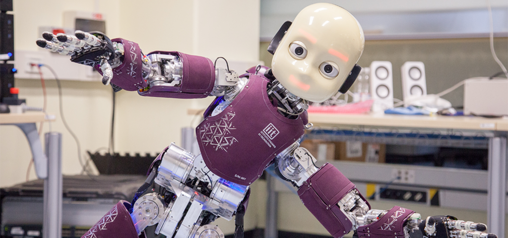iCub, il robot umanoide sviluppato dall'IIT, con il busto viola e il logo IIT, fotografato in un laboratorio di ricerca
