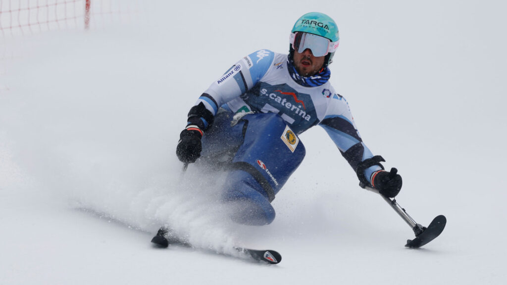 Atleta paralimpico in categoria Standing esegue una curva ad alta velocità sulla neve, con protesi all'arto inferiore visibile
