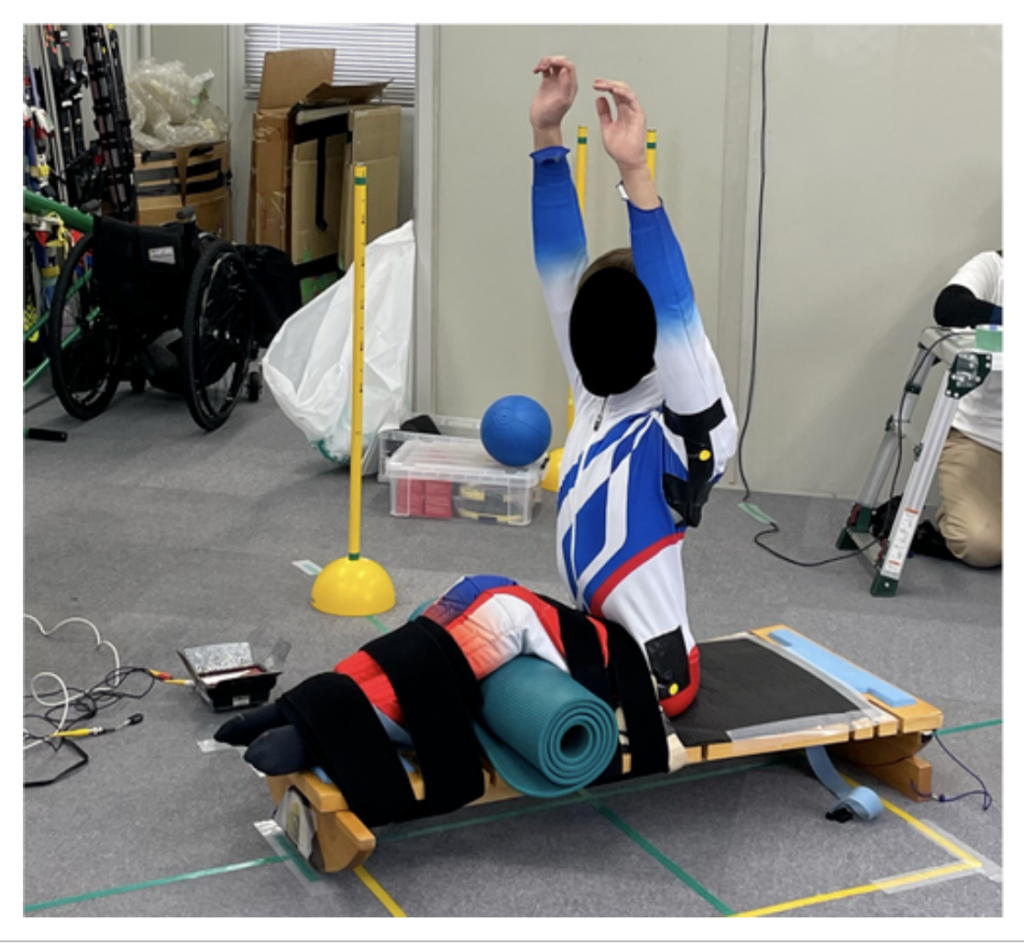 Atleta paralimpico seduto su una tavola piatta che esegue un test di estensione delle braccia verso l'alto per valutare forza e stabilità del tronco
