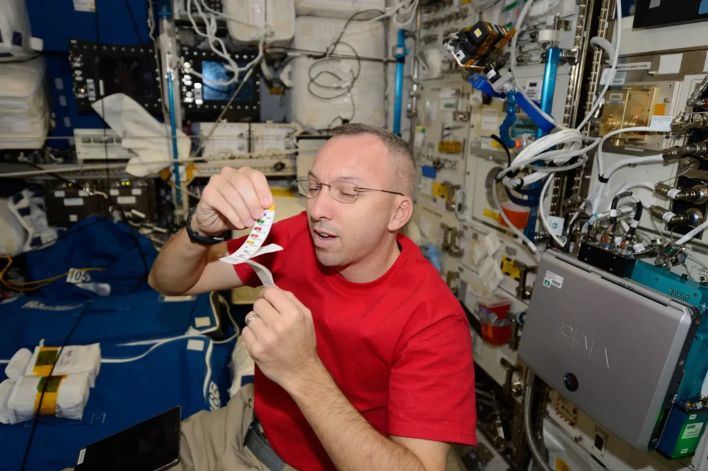 Astronauta osserva una striscia di carta con piccoli riquadri colorati per il campionamento della saliva
