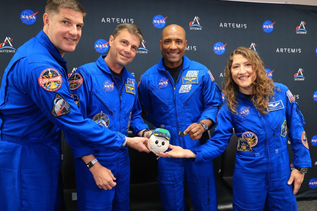 Gli astronauti in tute di volo blu sorridono mentre tengono tra le mani il piccolo peluche della mascotte Rise