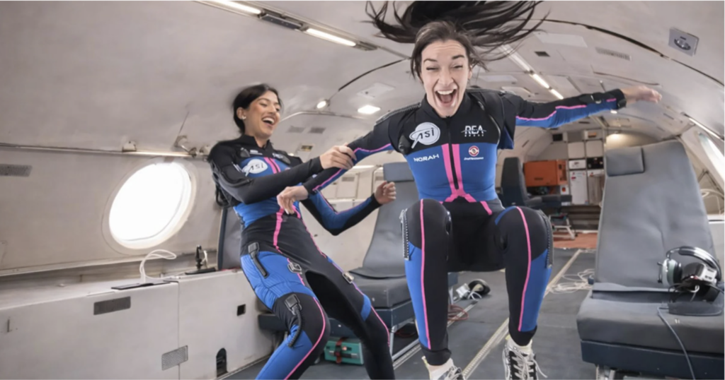 Shawna Pandya e Norah Patten in microgravità a bordo di un volo parabolico, indossando la biosuit EMSi di REA Space con loghi ASI visibili