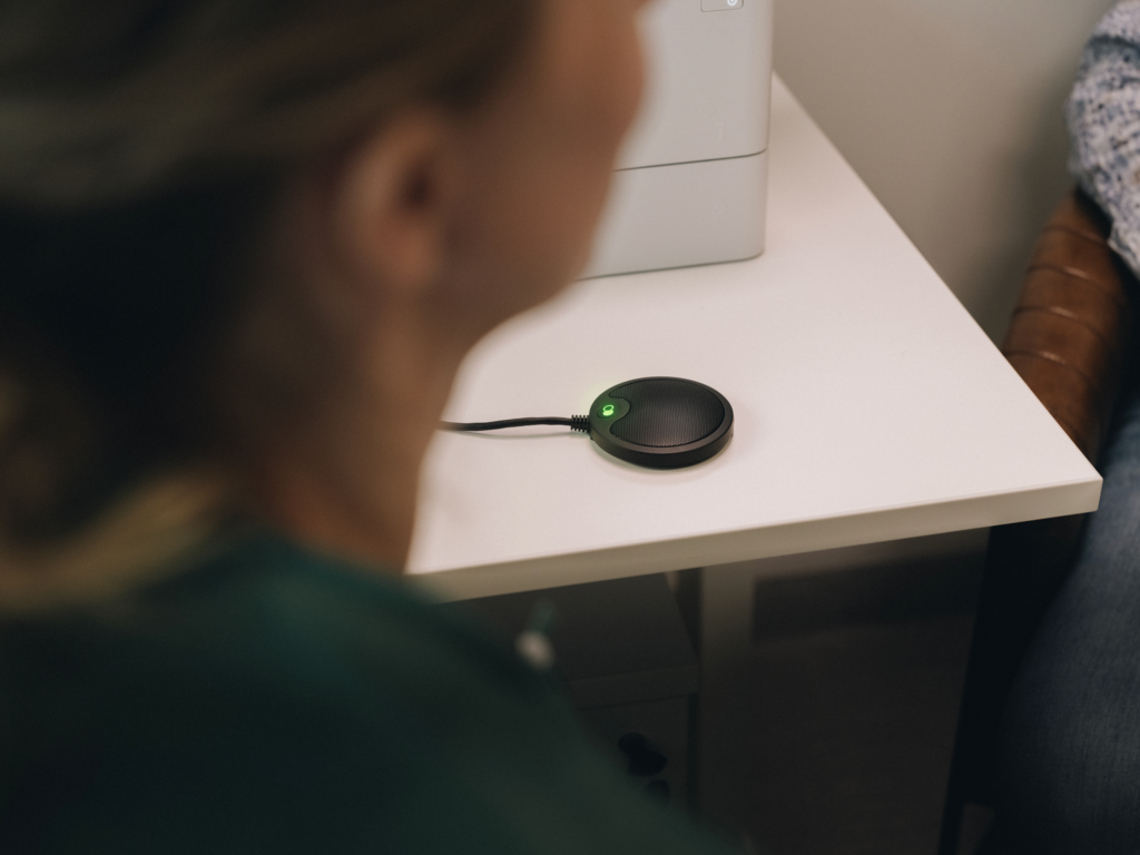 Microfono circolare nero con spia verde accesa posizionato su una scrivania bianca